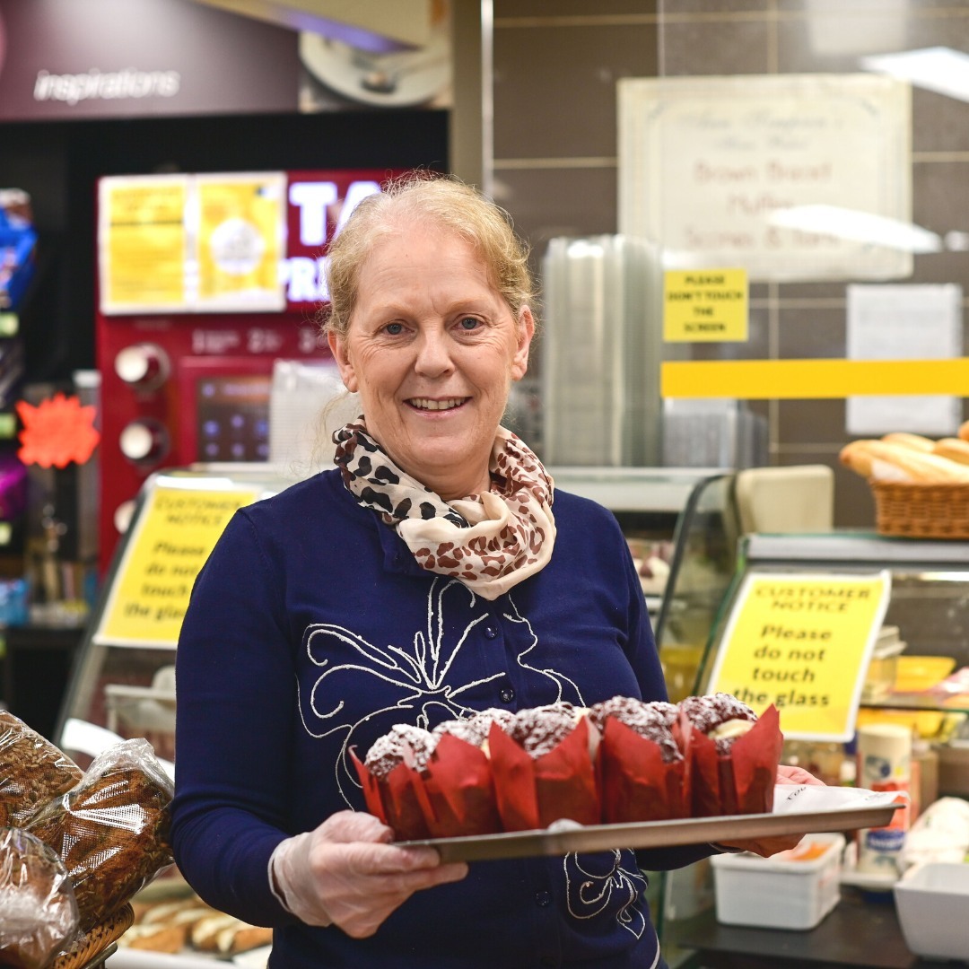 A member of the Simpson's Gala team holding a tray of freshly baked red velvet muffins beside the bakery counter