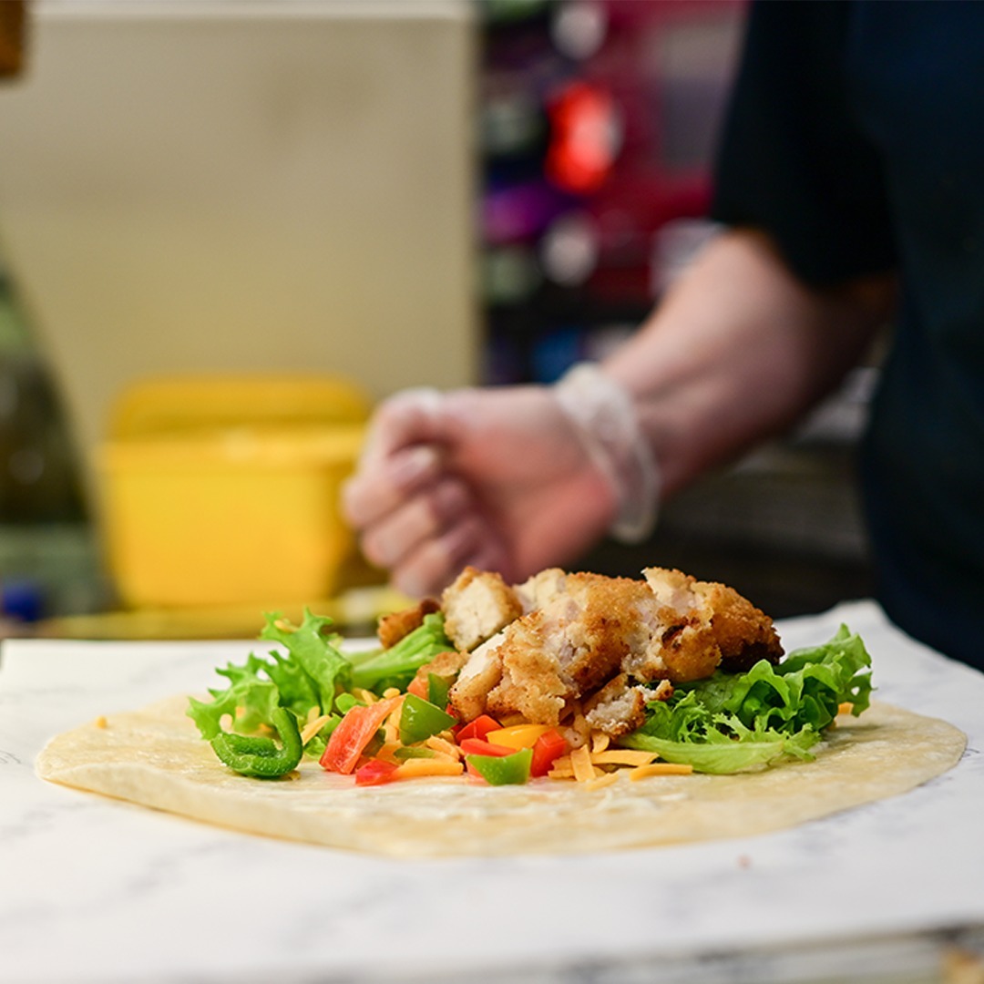 Chicken wrap being built with lettuce, peppers and grated cheese on a tortilla