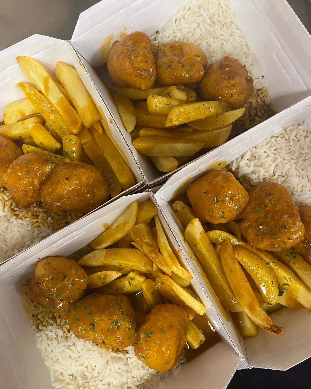 Four takeaway boxes of curry sauce chicken with chips and rice from the hot food counter