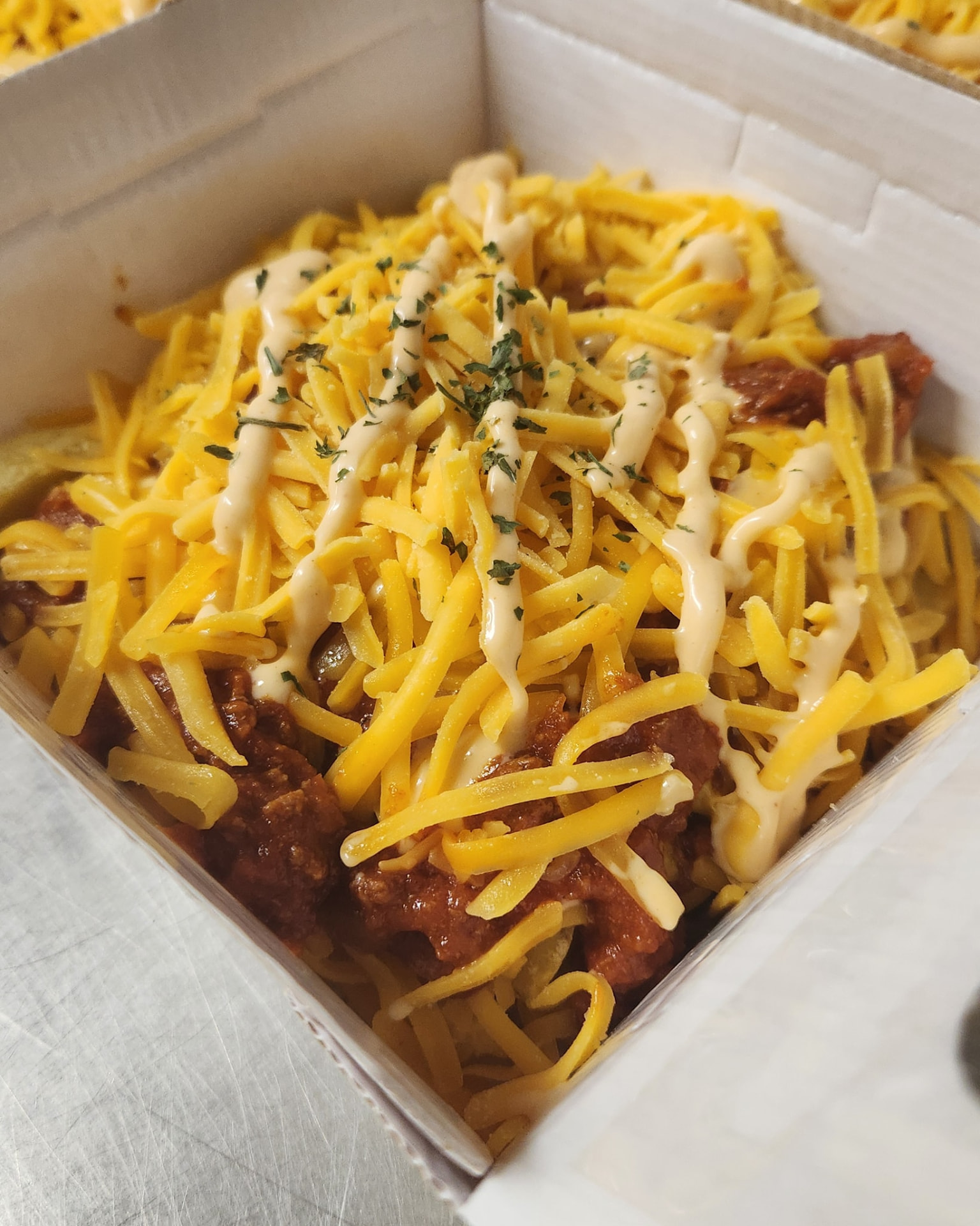 Takeaway box of chips loaded with chilli beef, grated cheddar, garlic sauce and parsley
