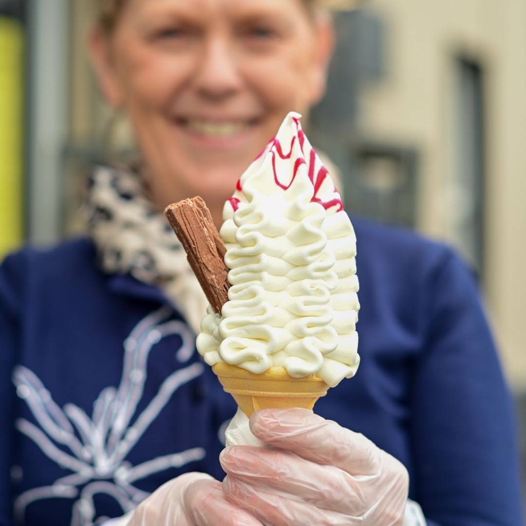 A 99 ice cream cone with a chocolate flake and raspberry sauce held up outside the shop