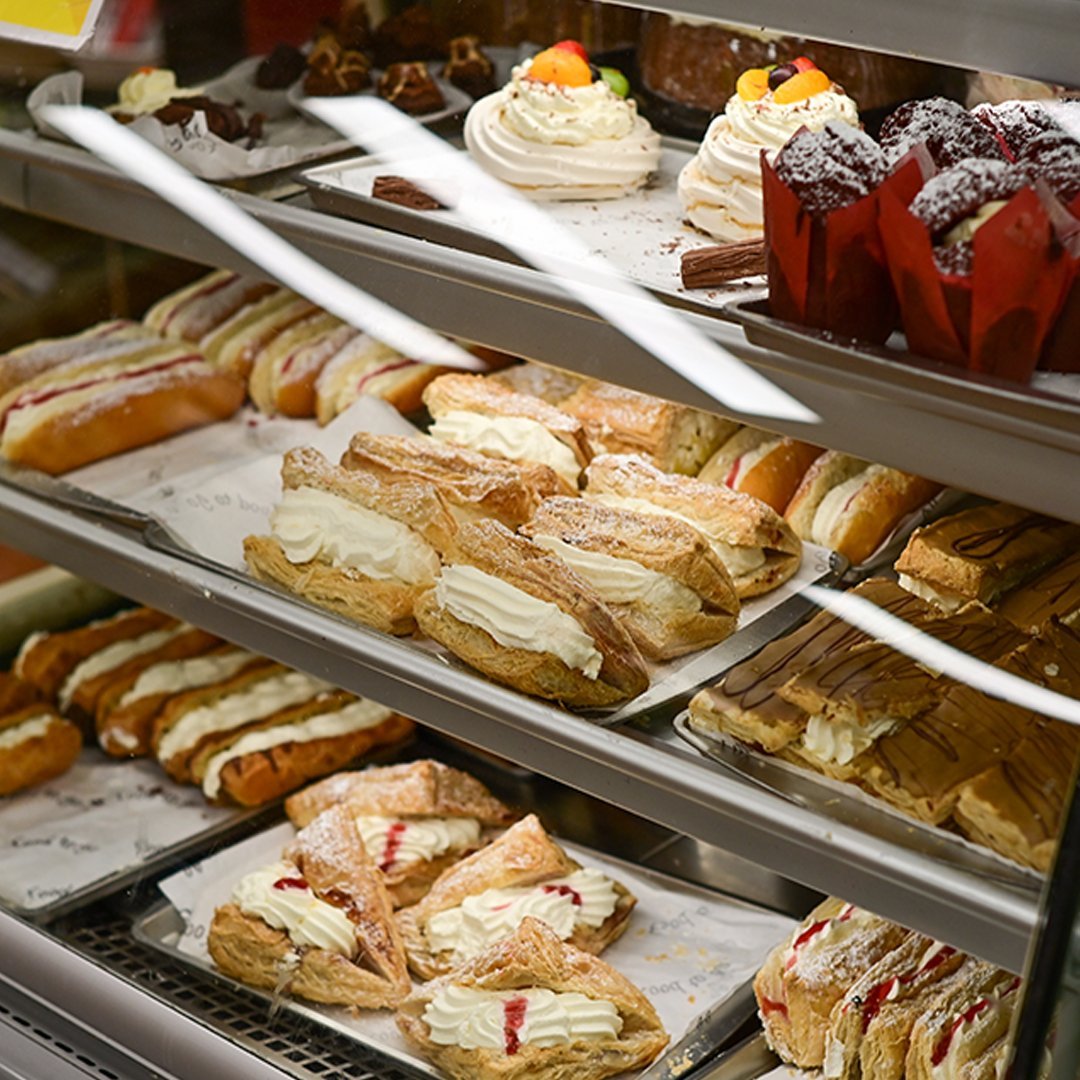 Bakery display shelves of fresh cream slices, eclairs, meringues and muffins