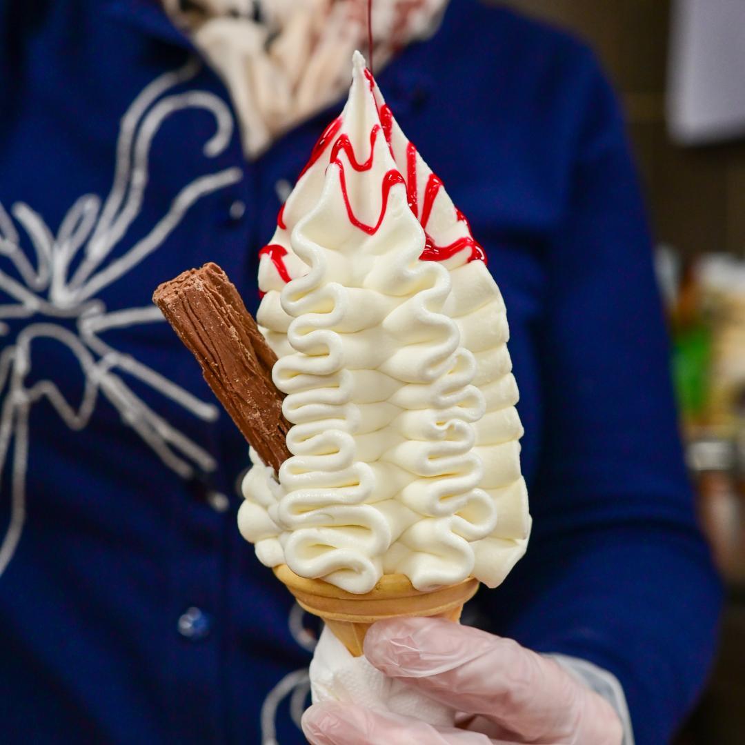 A 99 ice cream cone with a chocolate flake and raspberry sauce drizzle, held by a member of the Simpson's Gala team