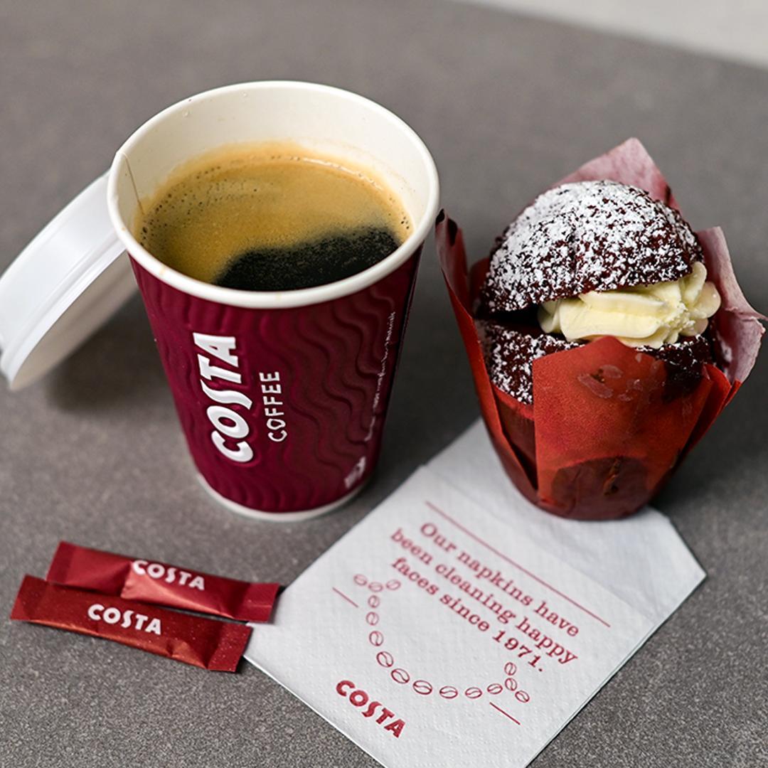 Costa Coffee cup of black coffee beside a red velvet muffin and sugar sticks