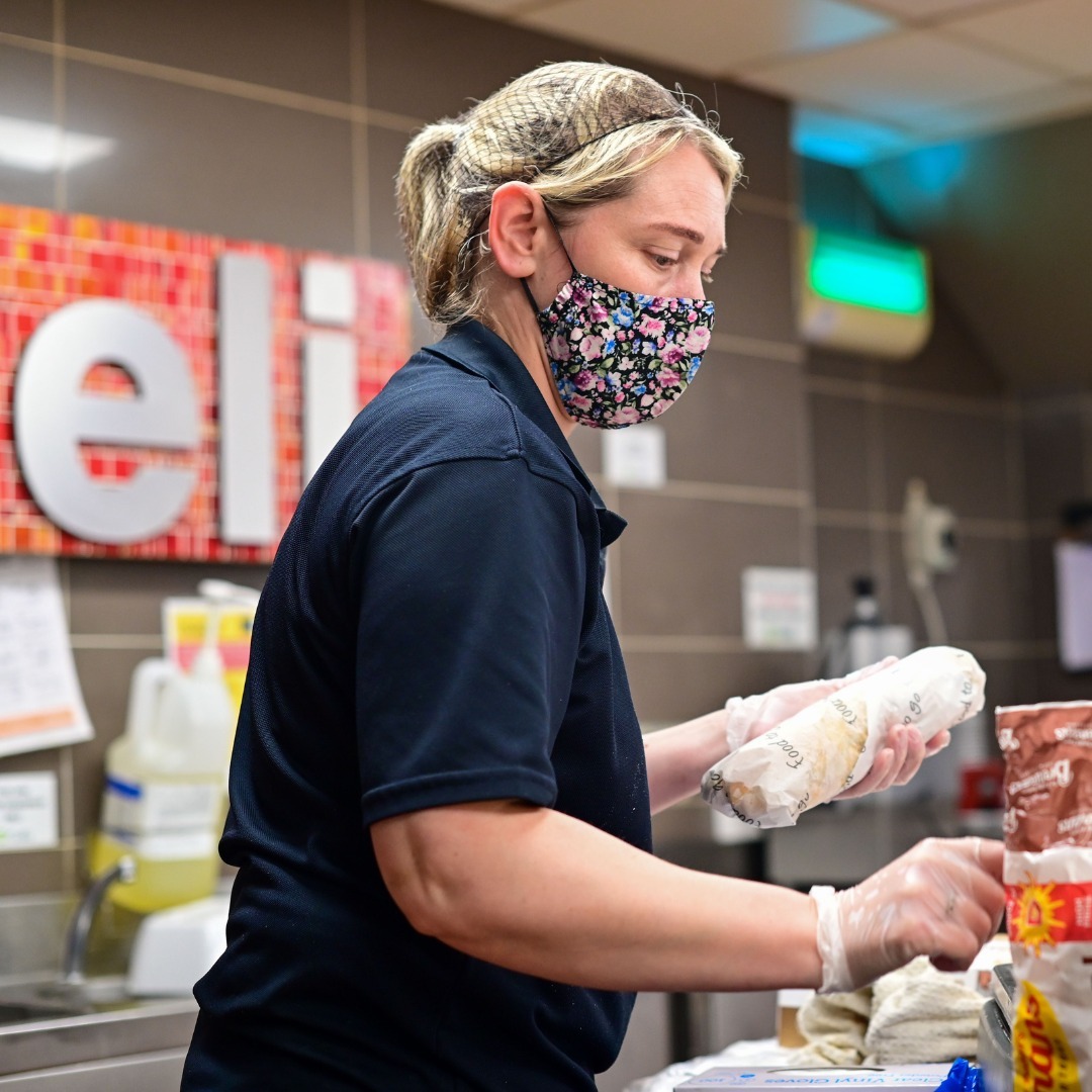 A member of the Simpson's Gala team wrapping a filled baguette in food to go paper at the deli counter